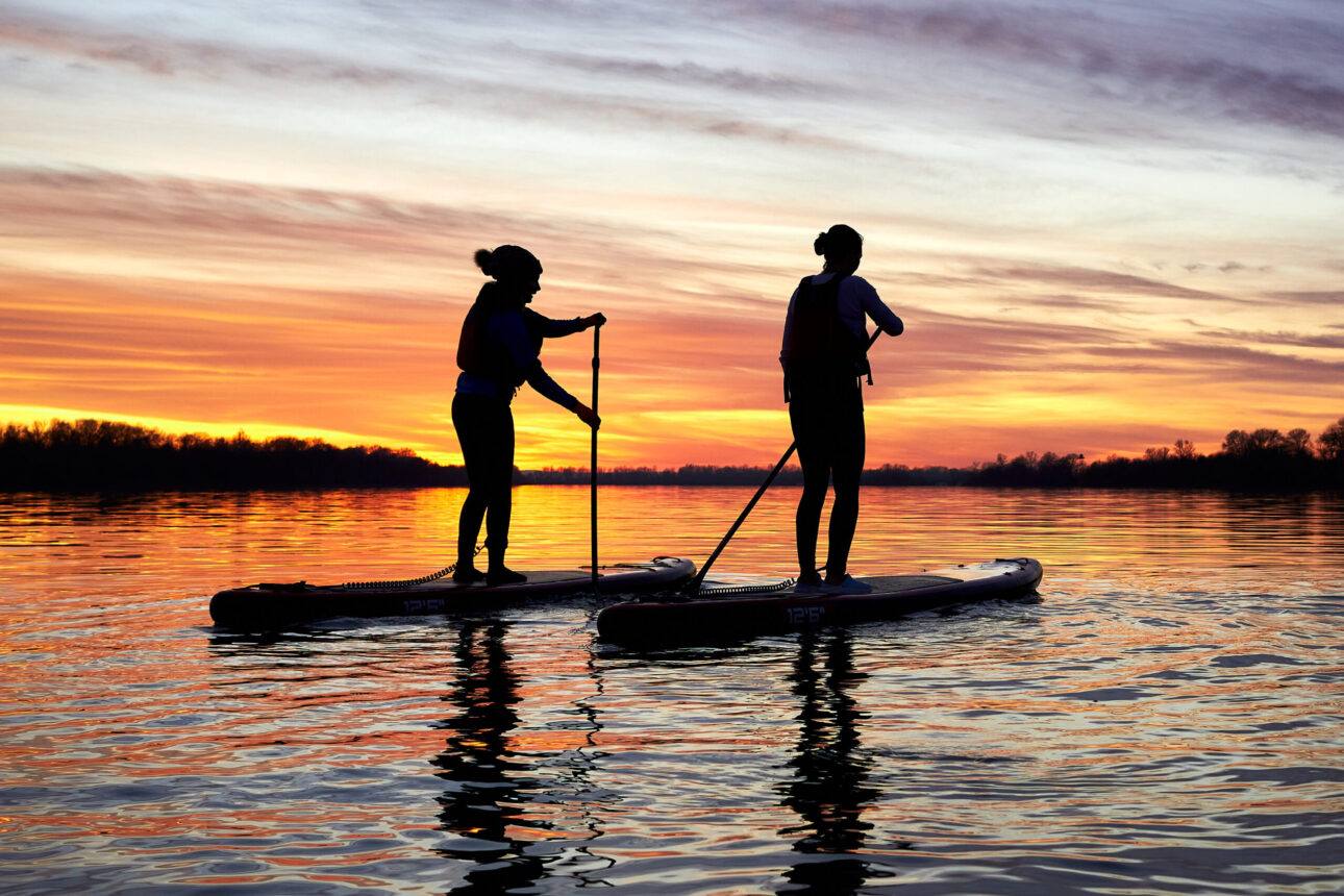 Zwei Stand-up-Paddler bei Sonnenuntergang auf dem See