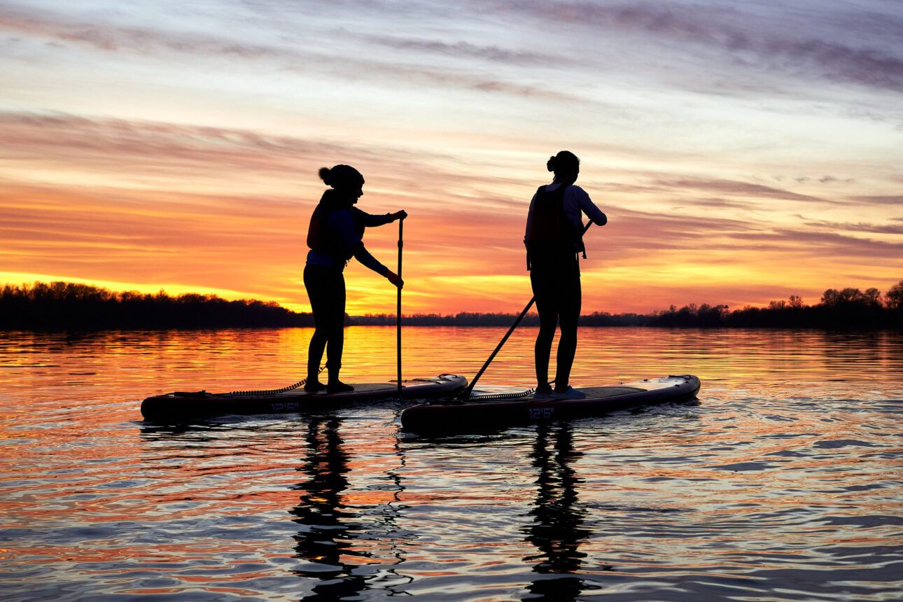 Zwei Stand-up-Paddler bei Sonnenuntergang auf dem See