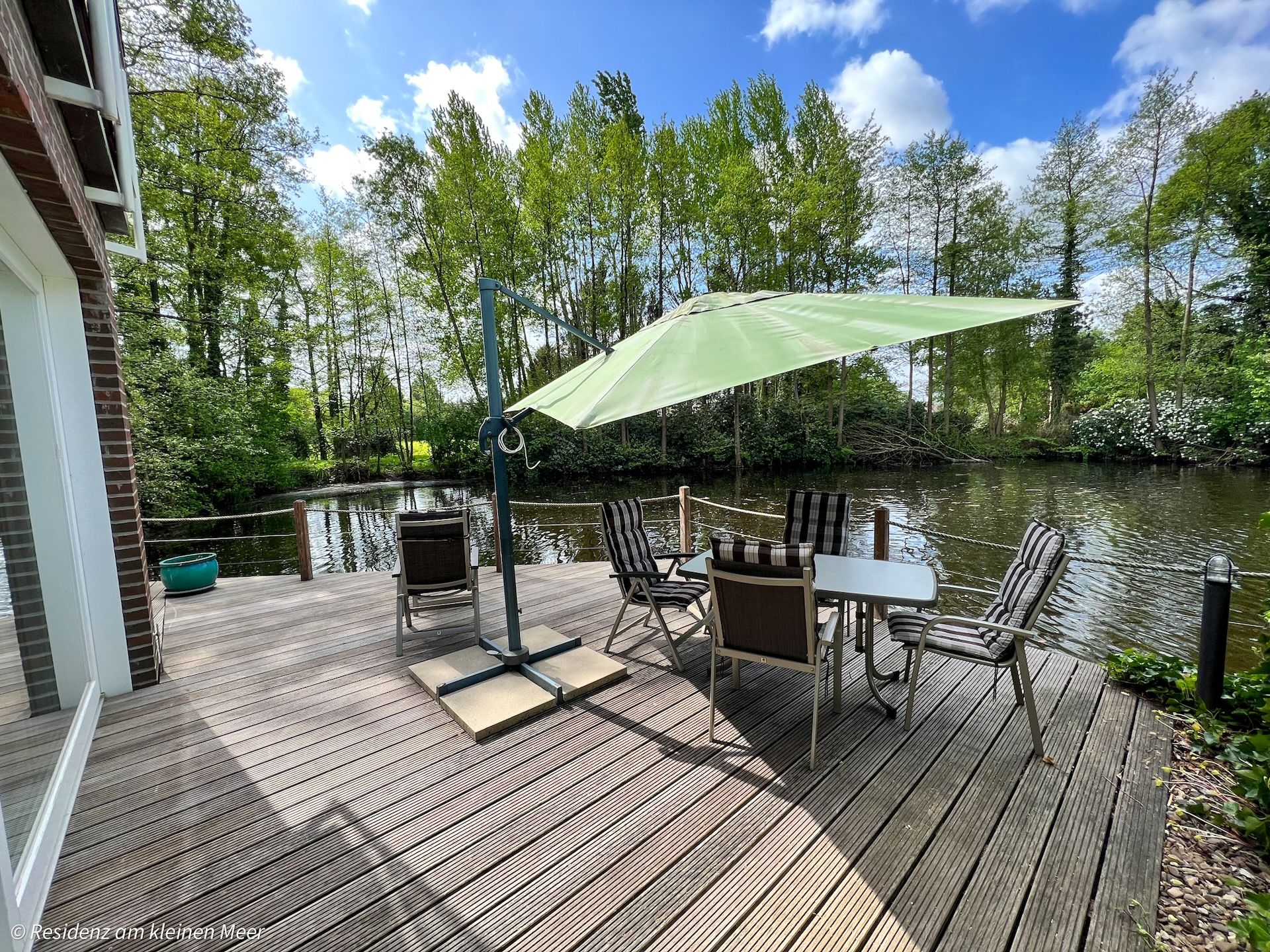 Holzterrasse mit Sitzgruppe und Sonnenschirm direkt am Wasser der Residenz am kleinen Meer