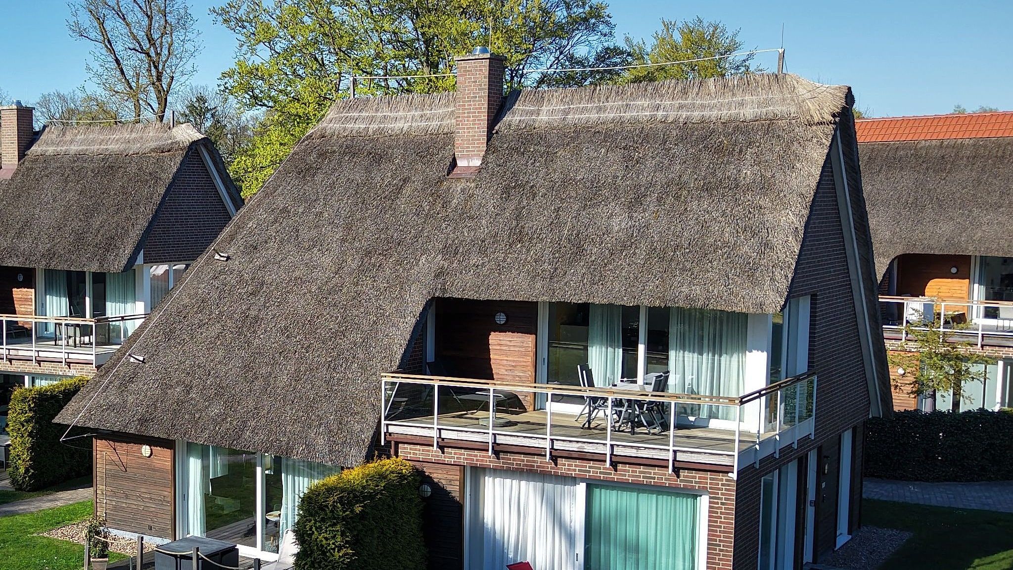 Luftaufnahme: Penthouse Wellenreiter mit großem Balkon unter dem Reetdach von Haus Wasser, Blick zum See